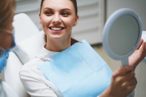 Patient holding mirror and smiling after dental visit